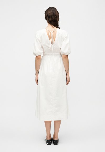 Λευκό midi φόρεμα με φουσκωτά μανίκια, ελαστική μέση και ανοιχτή πλάτη με δεσίματα. Λείο ύφασμα και μίνιμαλ διακοσμητικές λεπτομέρειες.