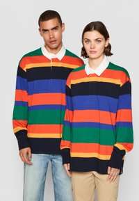 Bomulds langærmede polo-shirts med vandrette striber i rød, orange, gul, grøn, blå og sort med kontrasterende hvide kraver.