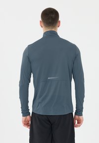 Långärmad, mörkblå träningsskjorta med hög krage, texturerad tyg och reflekterande detalj på baksidan. Slimmad passform och lätt design.
