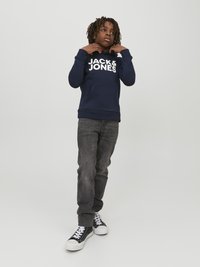 Mornarsko modra kapuca s spuščeno kapuco z belim logotipom "JACK & JONES", sprednjim žepom in rebrastimi manšeti, v kombinaciji s temno sivo jeans hlačami in črnimi visokimi supergami.