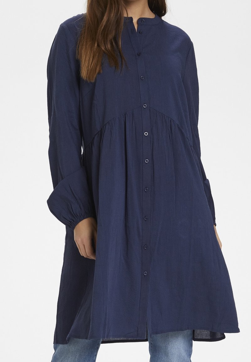 Robe boutonnée bleu marine en tissu texturé, avec manches longues, col montant et silhouette fluide à taille froncée.