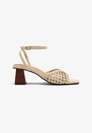 Sandale à talon bloc ouvert en beige. Caractérisée par une tige tressée, une sangle de cheville avec boucle et un semelle intérieure ergonomique. Talon bloc en bois.
