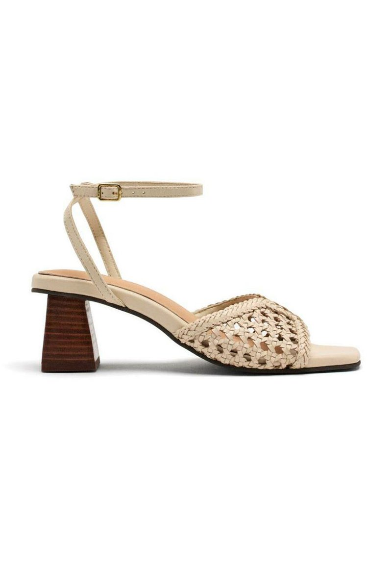 Sandalia de tacón bloque abierto en color beige. Cuenta con un upper trenzado, correa en el tobillo con hebilla y plantilla contorneada. Tacón de madera.