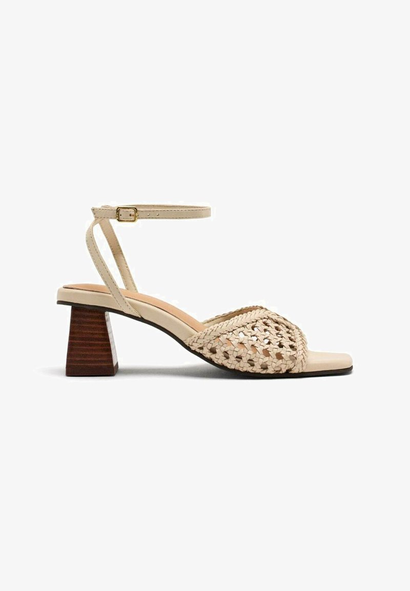 Sandalia de tacón bloque abierto en color beige. Cuenta con un upper trenzado, correa en el tobillo con hebilla y plantilla contorneada. Tacón de madera.