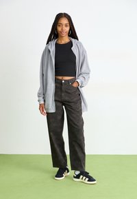 Pilka zip-up suknelė, juodas trumpas marškinėlis, raštuoti tamsūs kelnių, ir juodi sportbačiai su baltais ir auksiniais dryžiais. Lygi tekstūra, laisvas kirpimas.