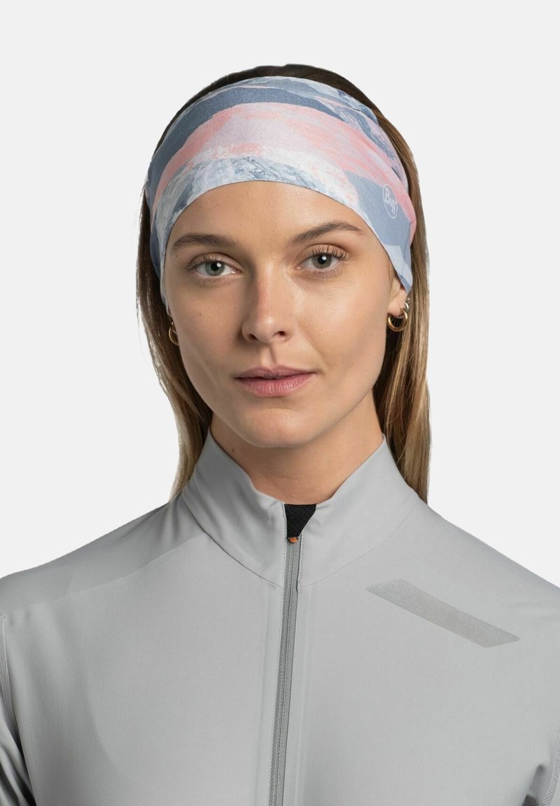 Diadema multicolor que presenta una tela suave y elástica con un patrón geométrico de rayas rosas, blancas y azules; llevada en la cabeza de un modelo.