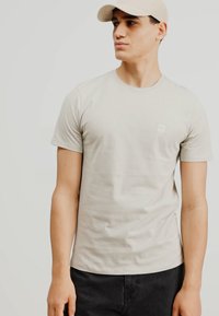 Svetlosivý tričko s krátkym rukávom vyrobené z mäkkej látky; okrúhly výstrih, priliehavý strih, s malou nášivkou loga na ľavom prsníku.