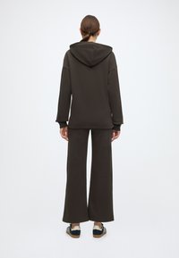 Καφέ φούτερ με μεγάλο κουκούλα και χαλαρή εφαρμογή, σε συνδυασμό με παντελόνι φαρδιάς γραμμής στο ίδιο χρώμα. Το υλικό έχει ομαλή και απαλή υφή.