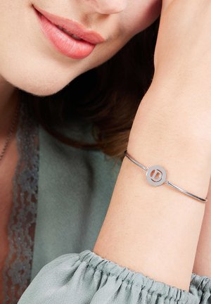 Zilveren bangle armband met een cirkelontwerp en een uitgesneden letter "D." Draagt om een pols, gecombineerd met een zachtgroen blouse.
