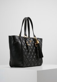 Black leather tote bag with diamond quilt pattern, gold hardware, dual handles, and a decorative tassel detail on the side.