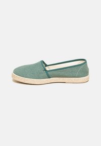 Green woven textile slip-on shoe with a jute rope sole and beige accents. Rounded toe and low-cut design.