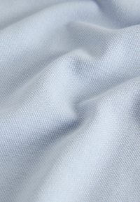 Posnetek iz bližine mehke, svetlo modre tkanine s fino teksturirano prejo in nežnimi gubi, ki ustvarjajo subtilne sence.