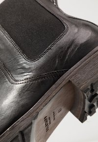 Bottine en cuir noir avec une texture douce, un panneau latéral élastique et un talon en bois doté d'une semelle extérieure crantée en caoutchouc noir.