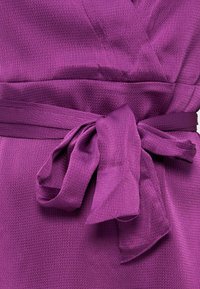 Μωβ ύφασμα με υφή δεμένο σε φιόγκο γύρω από τη μέση, με ορατή ραφή και πτυχώσεις στο υλικό.