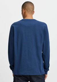 Navy kék, hosszú ujjú póló, puha anyagból készült, kerek nyakkivágással és laza szabással, a vállainál látható varrással.