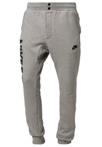Grå sweatpants av mjukt material, med en snäv design, elastisk midja, två knappstängningar och en svart Nike-logotyp på sidan.