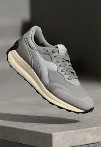 Baskets de sport grises avec une tige texturée, des accents lisses et une épaisse semelle de couleur crème. Comprend des lacets assortis et un détail de logo.