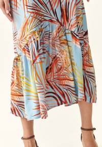 Robe fluide bleue avec un imprimé de feuilles de palmier vibrant en orange, jaune et rouge. La jupe a un ourlet superposé et volanté pour ajouter de la texture.