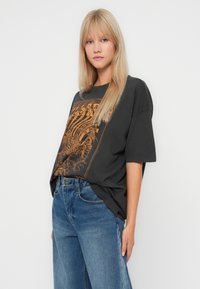 Zwarte oversized t-shirt met een oranje skelet grafisch ontwerp. Draag het met licht gewassen denim jeans, wat een casual pasvorm en stijl laat zien.