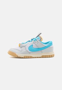La sneaker low-top di Nike presenta una tomaia in pelle grigia e blu, dettagli in mesh testurizzato, suola in gomma chiara e lacci blu a contrasto.