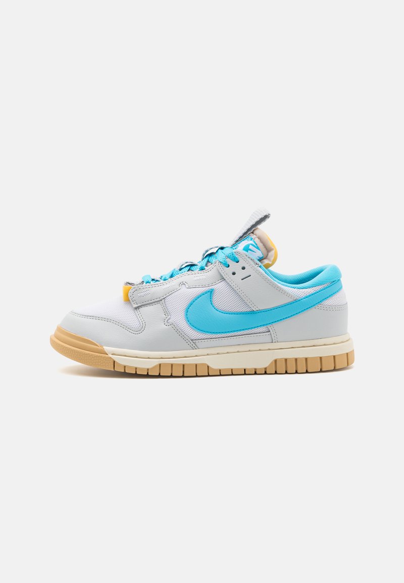 La sneaker low-top di Nike presenta una tomaia in pelle grigia e blu, dettagli in mesh testurizzato, suola in gomma chiara e lacci blu a contrasto.