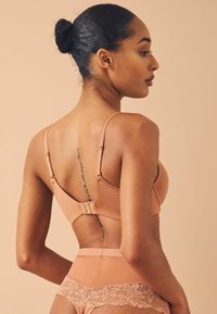 Completo intimo color nudo composto da reggiseno in tessuto liscio con spalline regolabili e chiusura con gancio, abbinato a slip a vita alta impreziositi da pizzo.