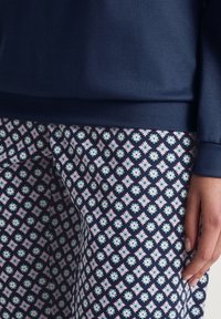Navy sweatshirt with ribbed cuffs paired with patterned trousers featuring a geometric floral design in pink, blue, and white on a dark background.