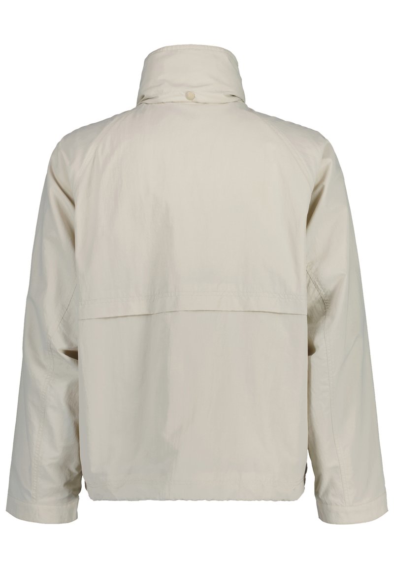 Veste légère beige avec manches longues, col haut avec bouton et détail de fente horizontale dans le dos.