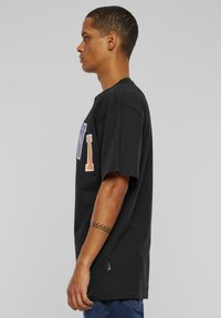Black cotton T-shirt featuring a large graphic on the front in orange and blue, short sleeves, and a relaxed fit. Textured surface, no patterns.