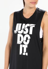 Sort med uden ærmer lavet af glat stof med en fed hvid grafik, der står "JUST DO IT." Udskæringer på siderne.