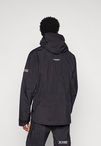 Casaco impermeável preto com capuz, apresentando zípers nas laterais, um logotipo nas costas e uma textura elegante e suave.