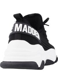Baskets de sport noires avec une tige en mesh texturé et une semelle en caoutchouc blanche, dotées d'une sangle arrière proéminente affichant "MADDEN" en lettres grasses.