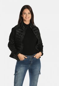 Doudoune noire avec un corps en tissu lisse et un devant matelassé. Associée à un pull noir et un jean en denim bleu avec des poches cargo.