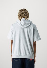 Sweatshirt à capuche gris clair avec des manches courtes, fabriqué en tissu doux. Présente une capuche spacieuse et une coupe décontractée.