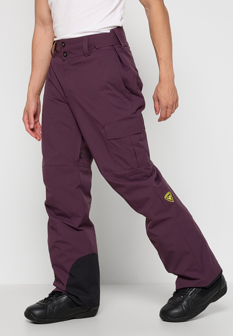 Pantaloni da neve bordeaux con taglio dritto, dotati di multeplici tasche e orlo inferiore nero. Realizzati in tessuto leggero e resistente.