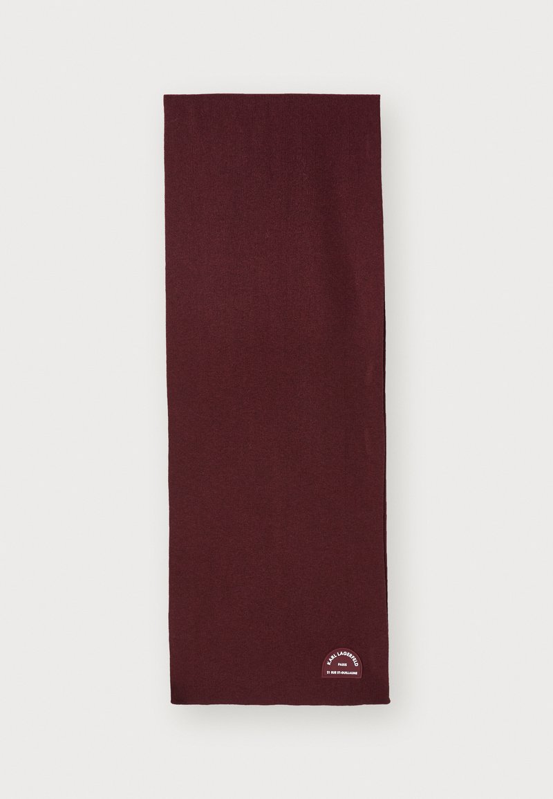 Cachecol bordeaux feito de material suave, em forma retangular, com um pequeno retângulo de logotipo branco no canto inferior. Textura lisa.