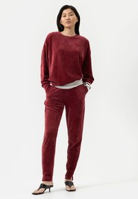 Bordeaux velours sweatshirt en bijpassende broek set, zachte textuur, losse pasvorm, zijzakken. Gecombineerd met zwarte open teen hakken.