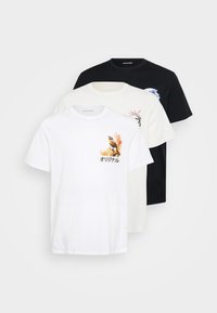Drie t-shirts gestapeld: één wit met een vogelillustratie, één crème met bloemmotieven en één zwart met een blauw ontwerp. Katoenen stof, korte mouwen.