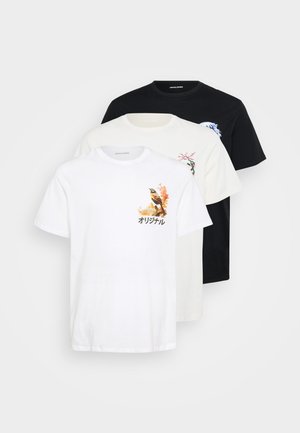 Drei übereinandergestapelte T-Shirts: eines in Weiß mit einem Vogelgrafik, eines in Creme mit floralen Details und eines in Schwarz mit einem blauen Design. Aus Baumwollstoff, mit kurzen Ärmeln.