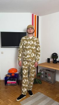 Σετ από λάδι-πράσινη ζακέτα και παντελόνι σε υφή. Στρογγυλός γιακάς, μακριά μανίκια και μαύρα παπούτσια χωρίς δέσιμο. Απλό καπέλο ολοκληρώνει την εμφάνιση.