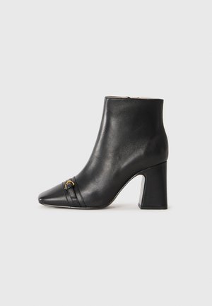 Black leather ankle boot with pointed toe, rounded heel, gold accent detail, and horizontal stripes across the front. Smooth texture.