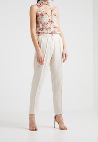 Bluzka bez rękawów w kwiatowy wzór z głębokim dekoltem w szpic, w zestawieniu z jasnobeżowymi spodniami o wysokim stanie. Modelka nosi cieliste sandały na wysokim obcasie.