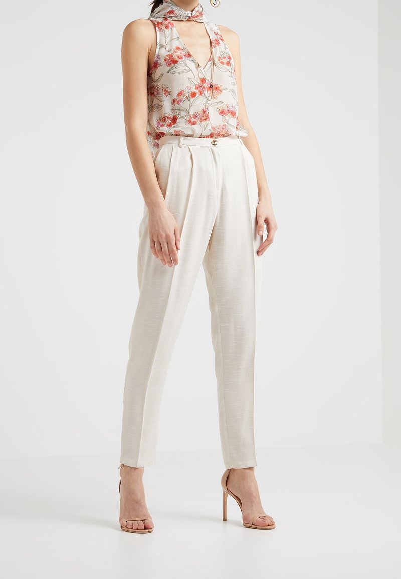 Bluzka bez rękawów w kwiatowy wzór z głębokim dekoltem w szpic, w zestawieniu z jasnobeżowymi spodniami o wysokim stanie. Modelka nosi cieliste sandały na wysokim obcasie.