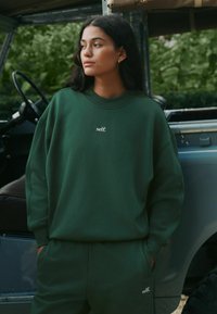 Zielona bluza i dopasowane spodnie o luźnym kroju. Na bluzie biały napis "self.", ściągacze na mankietach i miękka tekstura.