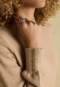 Bežs džemperis ar ribotām apkaklēm un aprocēm, ar trim zelta pogām uz aproces. Mīksta tekstūra un pieguļošs dizains.