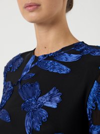 Svart klänning med strukturerad blå blommig broderi, rund halsringning och korta ärmar, som framhäver en kombination av material och designdetaljer.