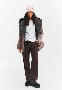 Kurtka puchowa w kolorze czarnym i stonowanym brązie, z wysokim kołnierzem i zatrzaskami. Połączona z brązowymi spodniami z kordurowej tkaniny oraz jasnoróżową czapką.