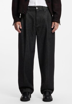 Pantalones de pierna recta de color gris oscuro con un patrón texturizado usados con zapatos negros, una camisa blanca y una chaqueta oscura.