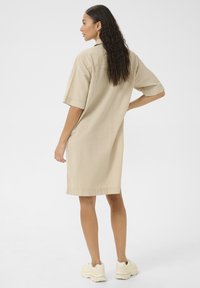 Randig beige skjortklänning med korta ärmar, en knappad krage och sidofickor, tillsammans med ljusa sneakers. Slät textur.