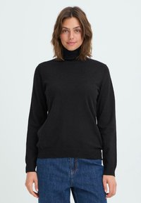 Schwarzer Rollkragenpullover aus weichem Strickstoff, mit langen Ärmeln und gerippten Bündchen und Saum. Getragen mit blauen Jeans.